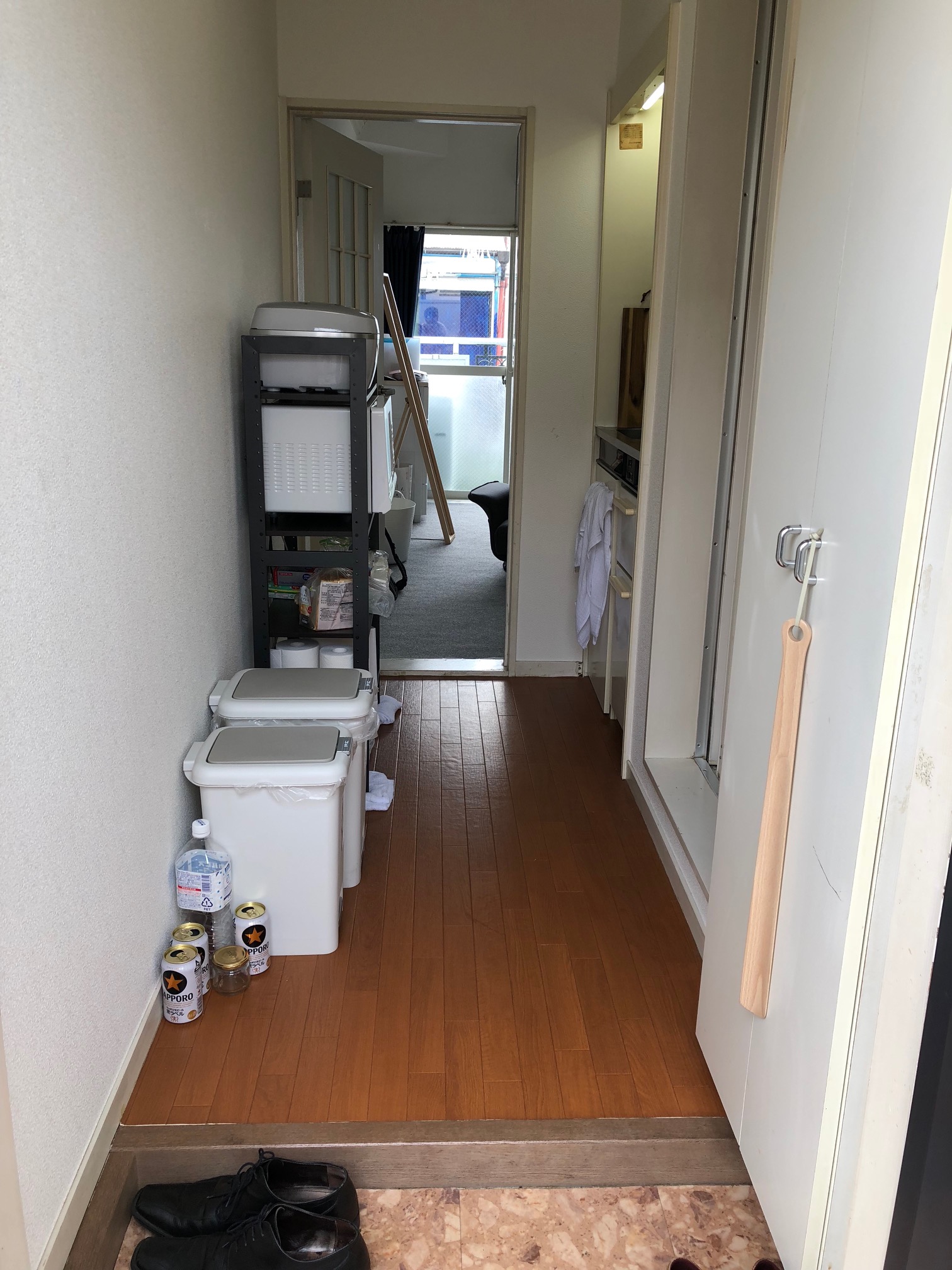 (Caption) Welcome home! This is the entrance hall with obviously wrongly placed shoes. From right to left, there’s a closet for shoes, entrance to the bathroom, kitchen so small that it took me two weeks just to find it, shelf with kitchen appliances, two trash cans and a lot of empty beer cans.